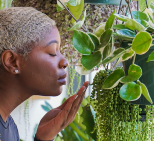 A blonde black woman gets close to her potted plants with closed eyes and a serene expression